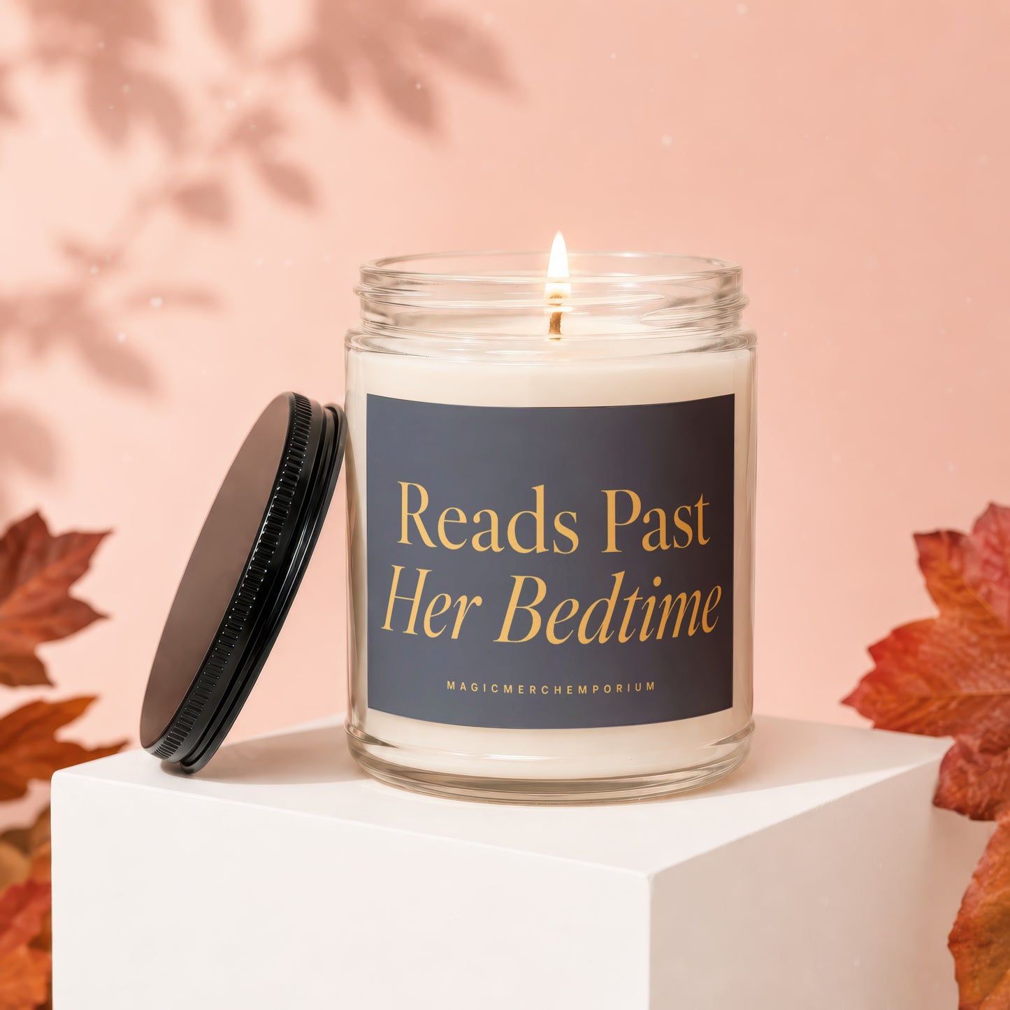 Glass jar candle with lit wick, reads "Reads Past Her Bedtime".