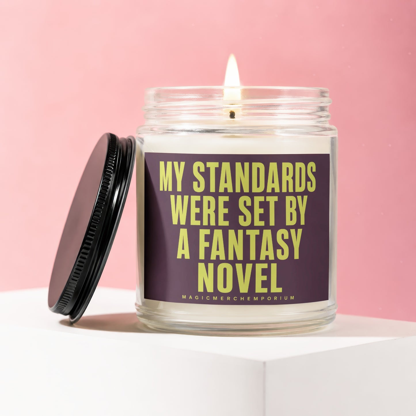 Glass candle with lit wick and black lid, labeled "My Standards Were Set By A Fantasy Novel".