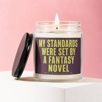 Glass candle with lit wick and black lid, labeled "My Standards Were Set By A Fantasy Novel".