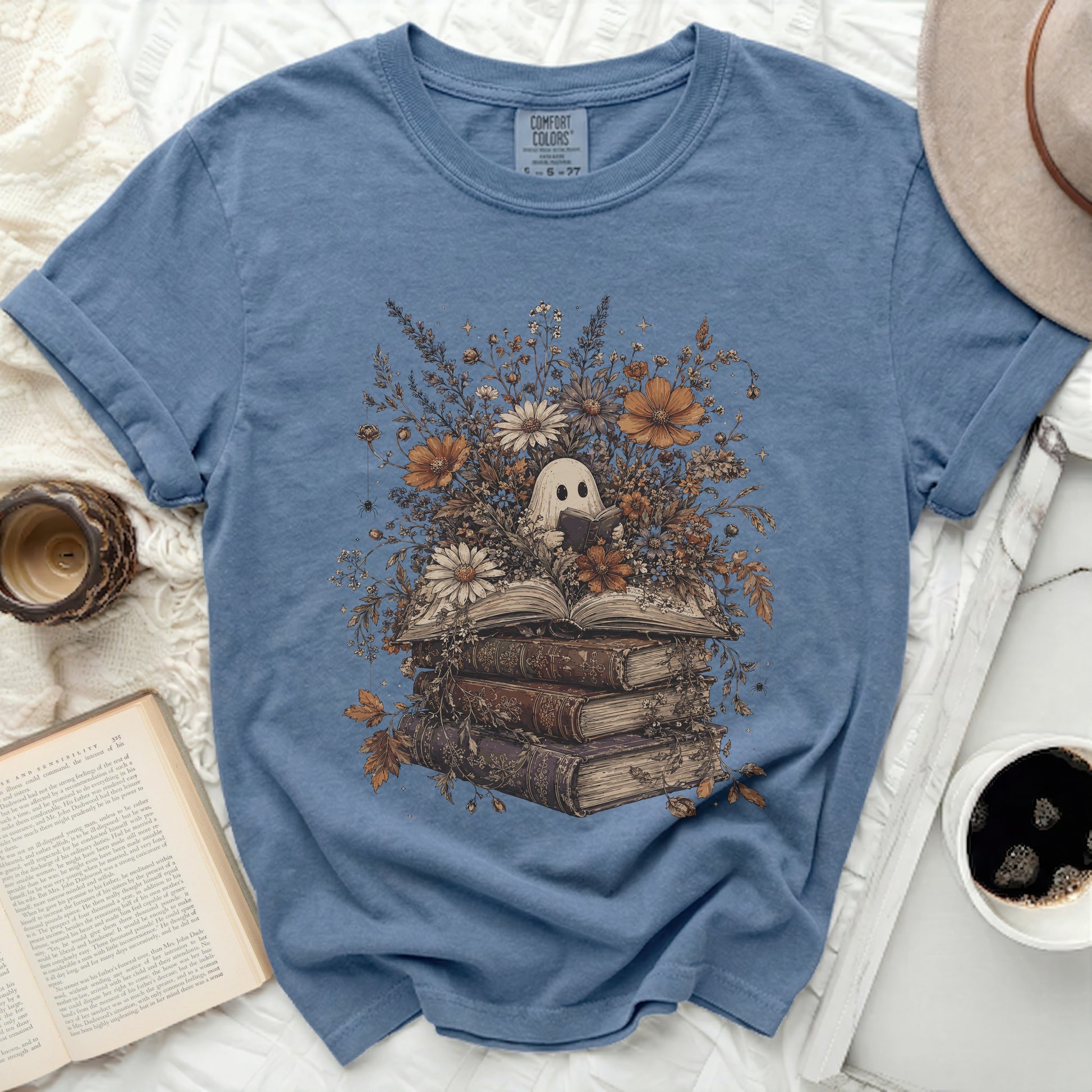 Blue t-shirt with a ghost reading a book among flowers and old books.