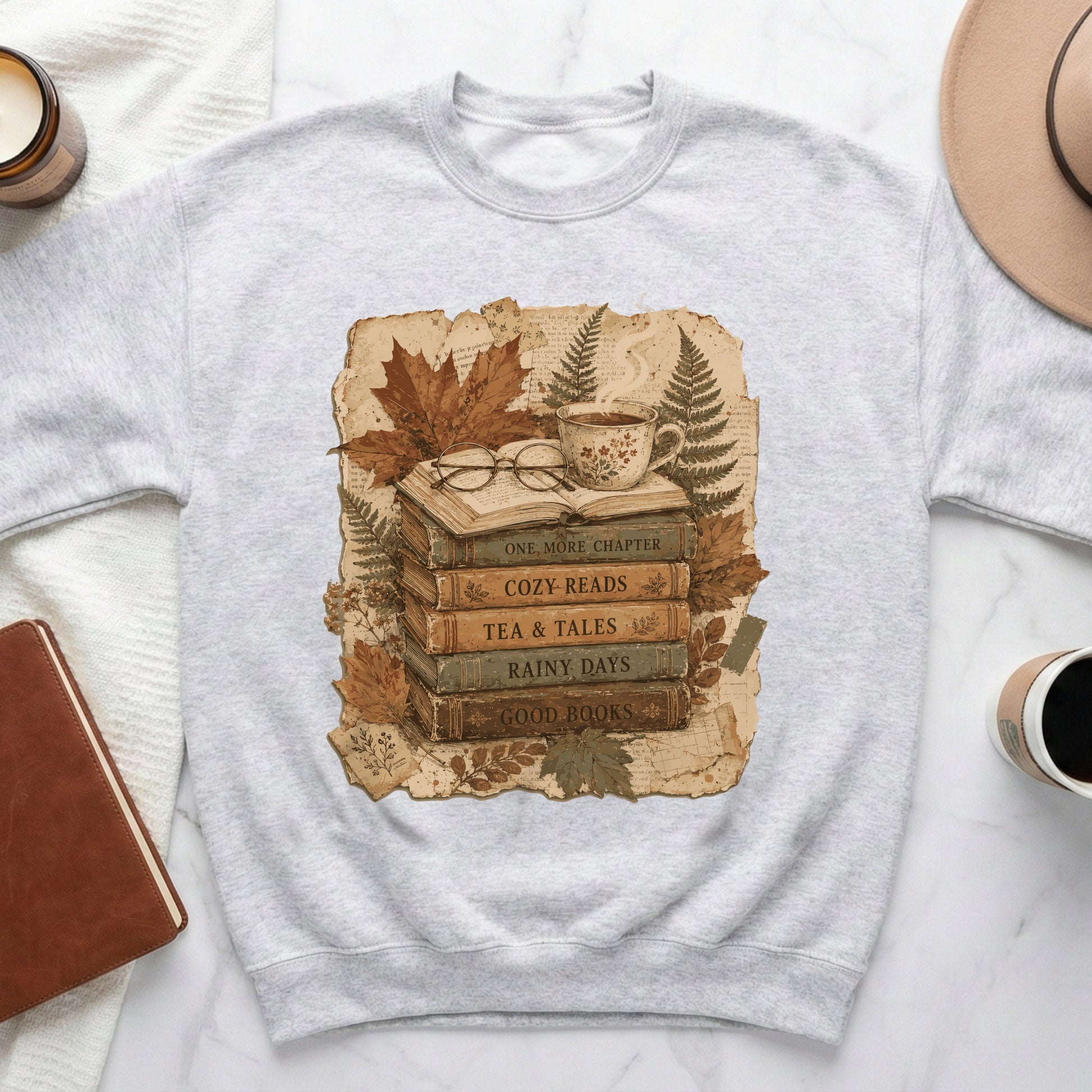 Gray sweatshirt with stacked books featuring text: "One More Chapter," "Cozy Reads," "Tea & Tales," "Rainy Days," "Good Books."