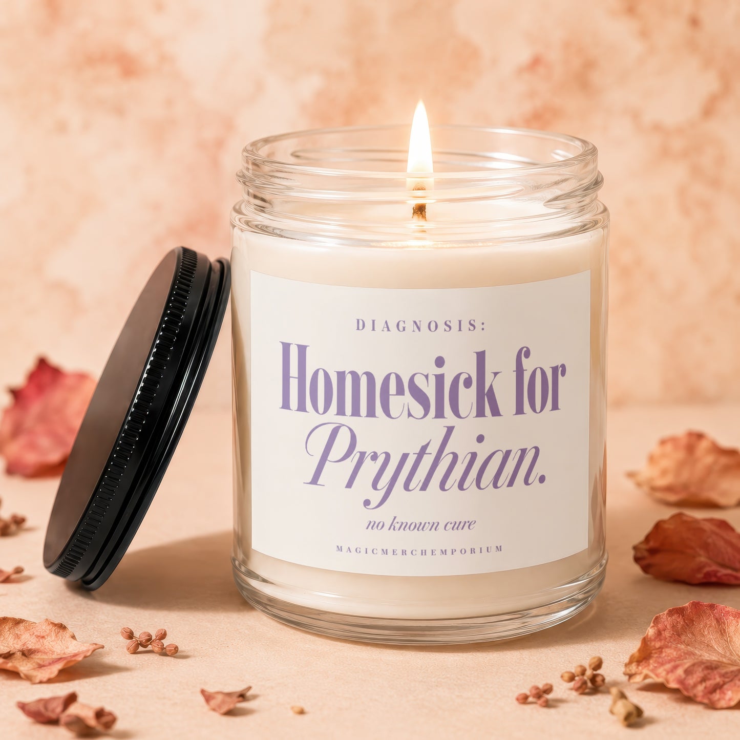 A lit white candle in a glass jar with a label reading Homesick for Prythian rests on a surface surrounded by dried rose petals.