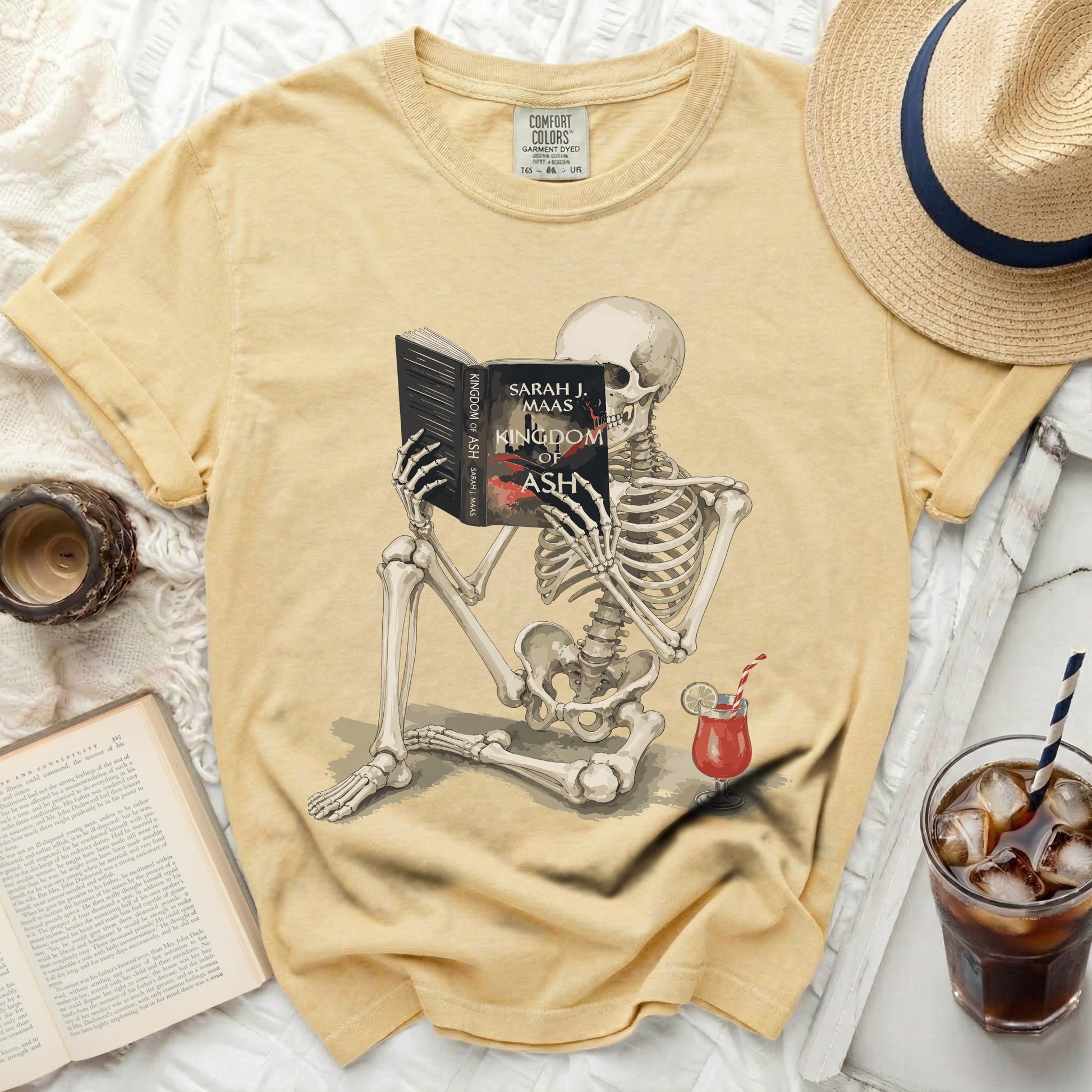 Skeleton reading "Kingdom of Ash" by Sarah J. Maas with a drink.