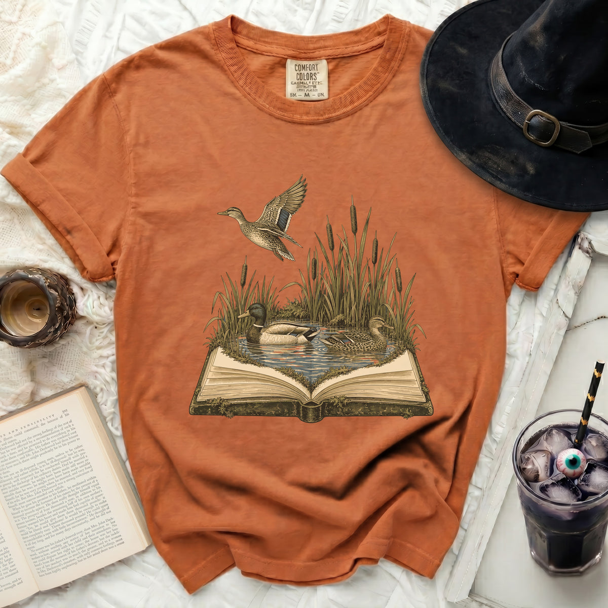Orange t-shirt with vintage illustration of ducks on an open book.