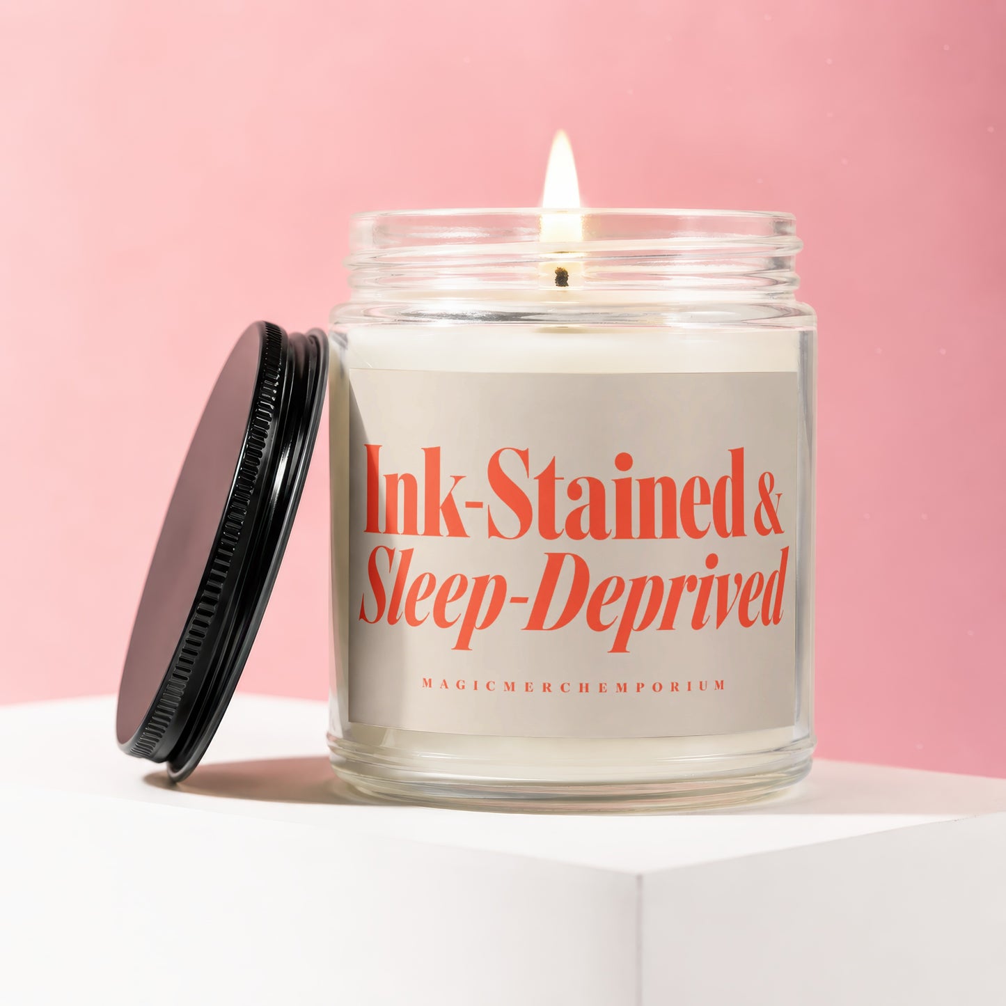 Jar candle with "Ink-Stained & Sleep-Deprived" text and a lit wick.