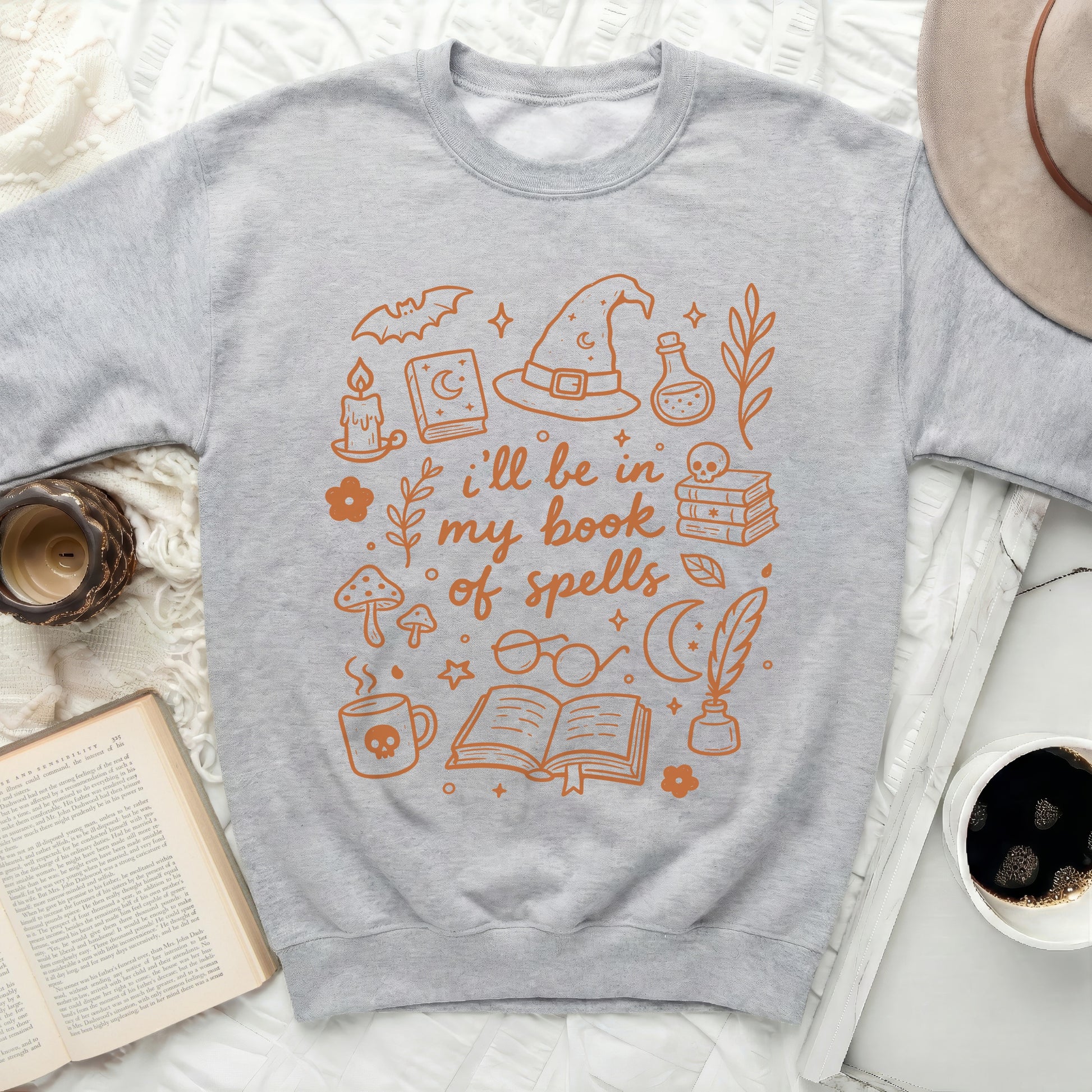 Sweatshirt with orange outline drawings of witchy items and the text "i'll be in my book of spells".