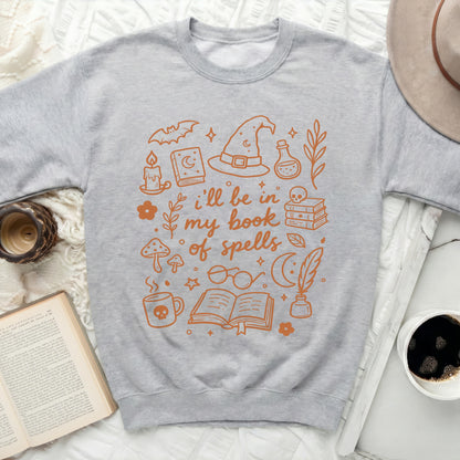 Sweatshirt with orange outline drawings of witchy items and the text "i'll be in my book of spells".