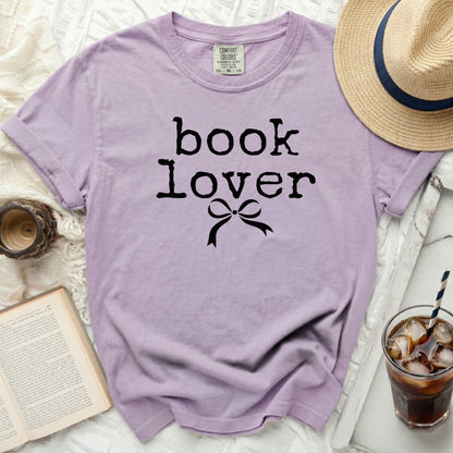 Purple t-shirt with "book lover" graphic and a bow, next to a book and drink.