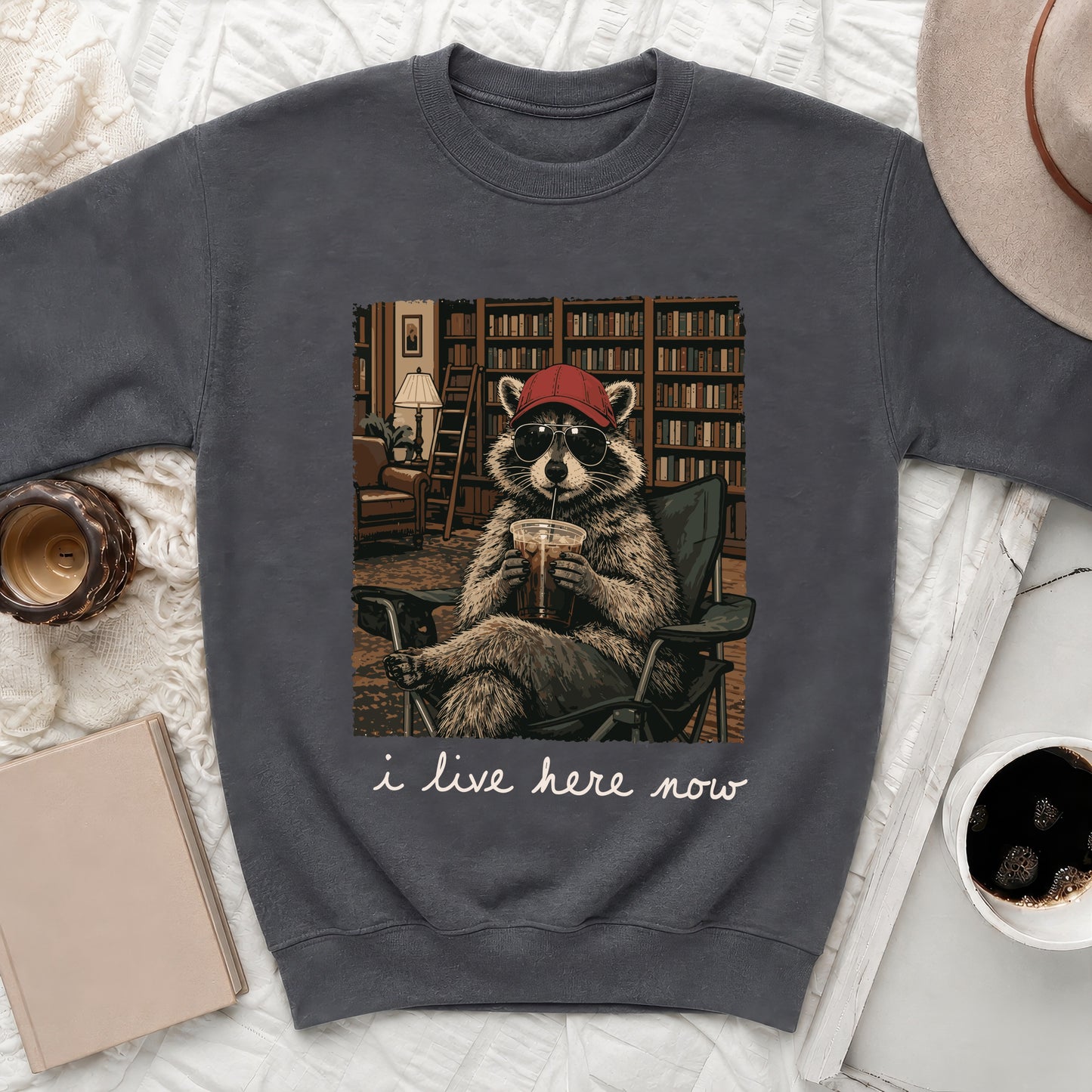 Raccoon in sunglasses and hat drinking beverage, with text "i live here now".