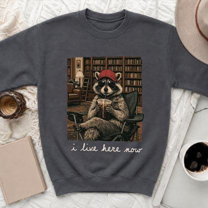 Raccoon in sunglasses and hat drinking beverage, with text "i live here now".