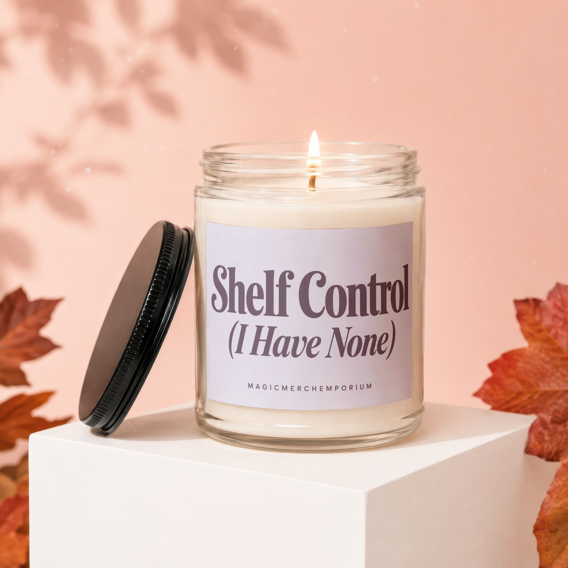 Glass jar candle with "Shelf Control (I Have None)" label, lit wick, and black lid.