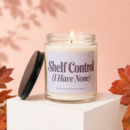 Glass jar candle with "Shelf Control (I Have None)" label, lit wick, and black lid.