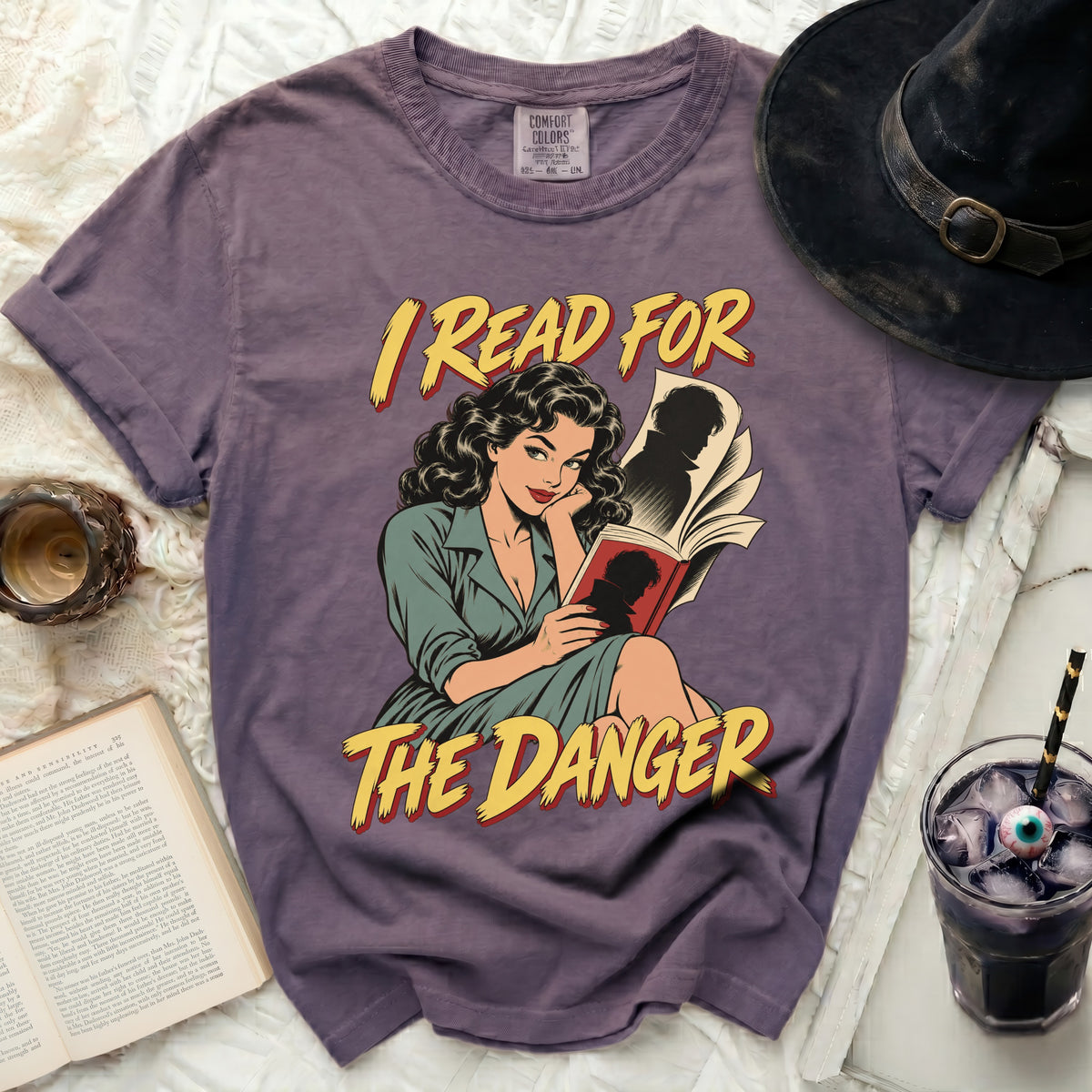 Purple t-shirt with comic illustration of woman reading and text "I READ FOR THE DANGER".
