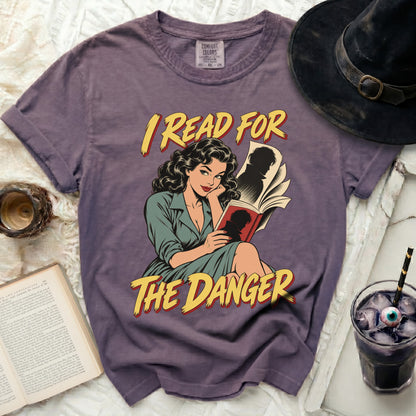 Purple t-shirt with comic illustration of woman reading and text "I READ FOR THE DANGER".