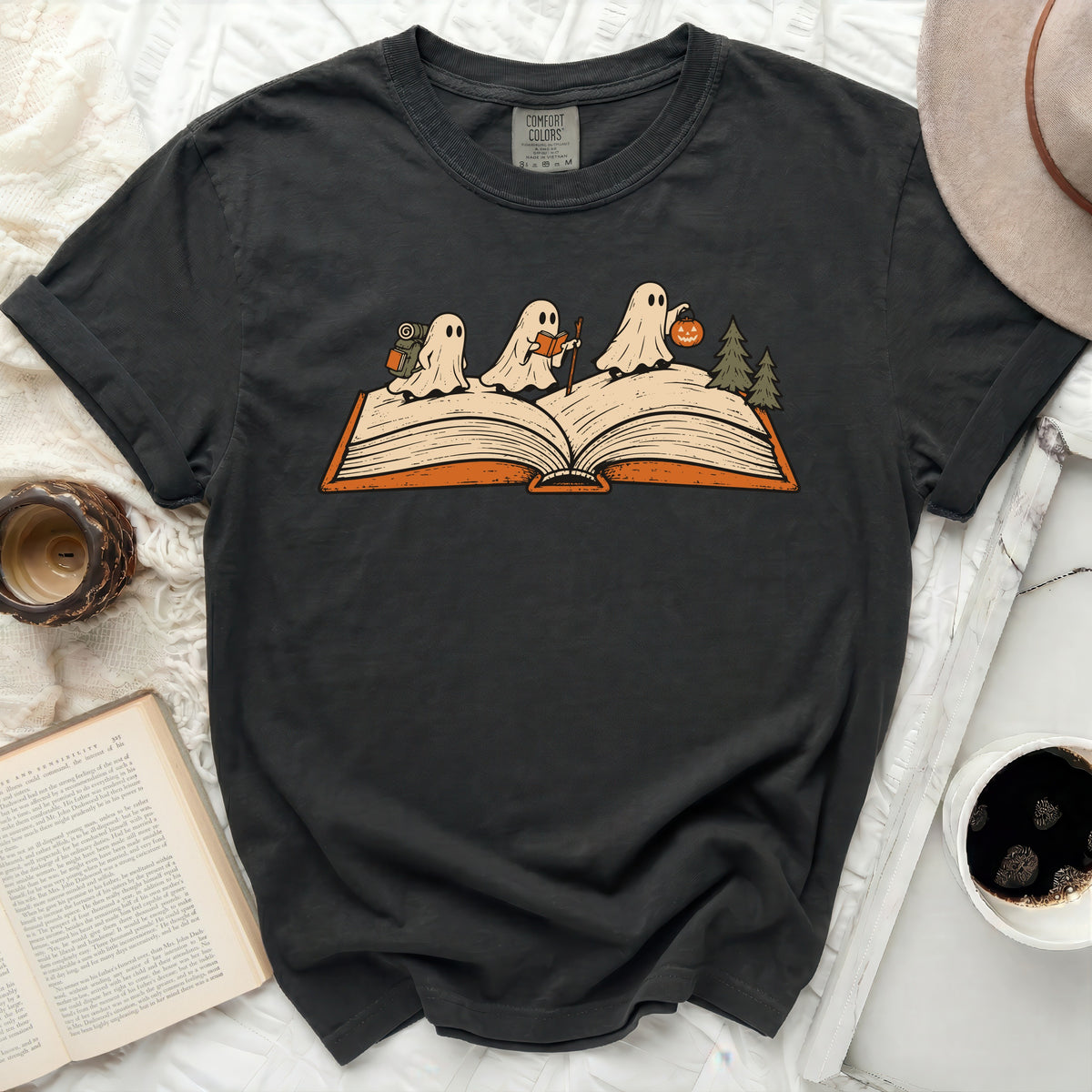 Ghost hikers on an open book with trees and a pumpkin, on a dark shirt.