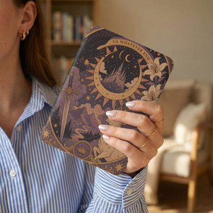 Person holds a book cover with celestial castle, crown, wolf, lily, and sword designs.