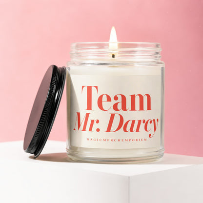 Glass candle with lit wick and black lid, labeled "Team Mr. Darcy."