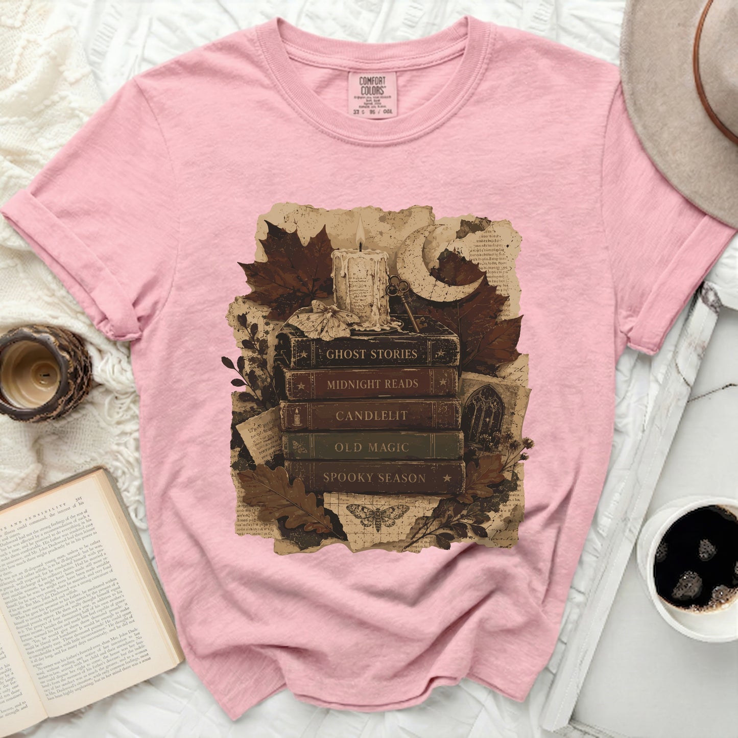 Pink t-shirt with a vintage illustration of books, candle, moon, and autumn leaves.