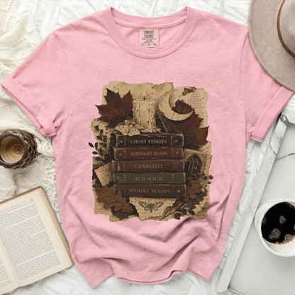 Pink t-shirt with a vintage illustration of books, candle, moon, and autumn leaves.
