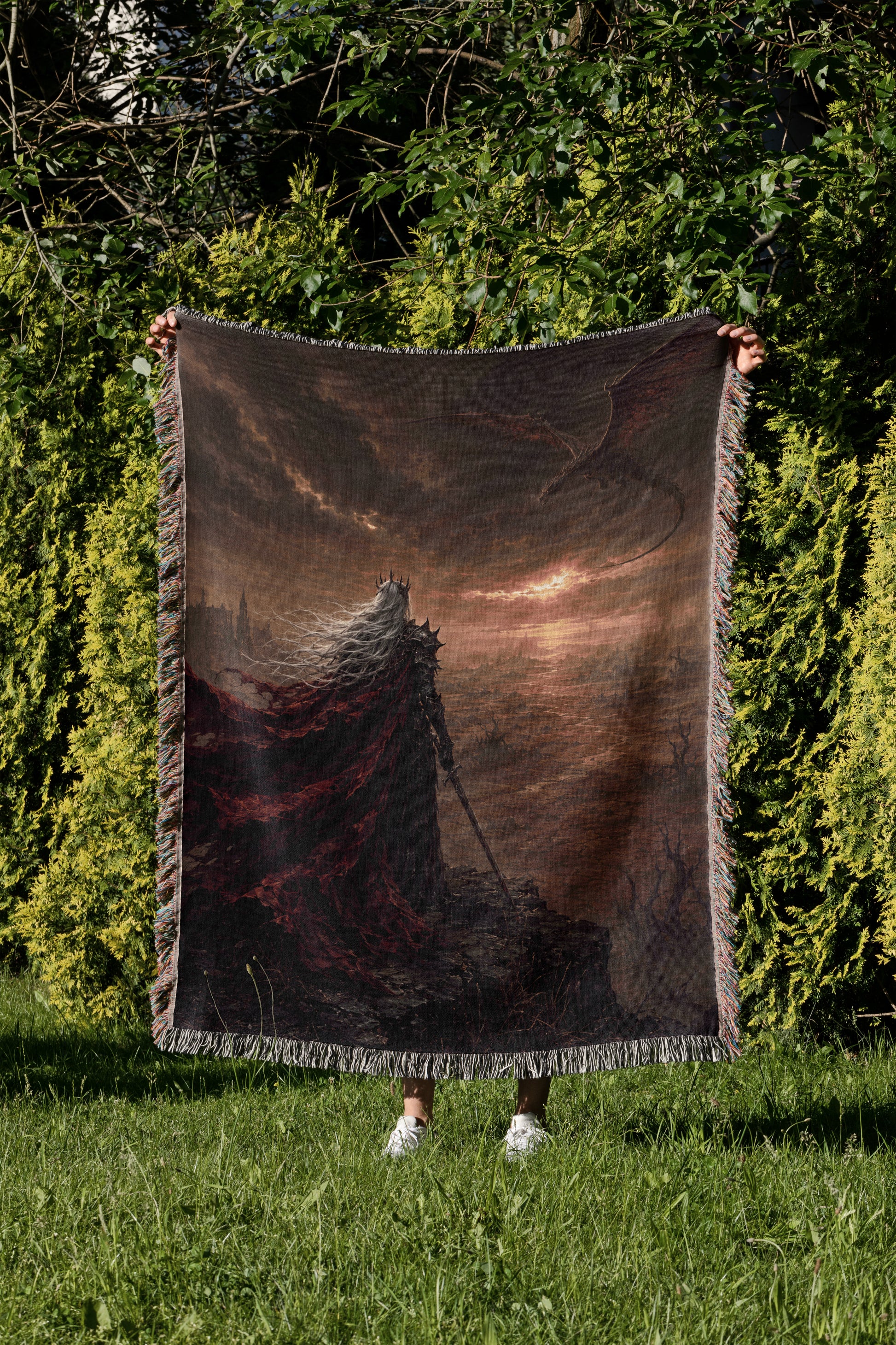 A person is holding a large, dark-colored blanket with a dragon design on it, standing in a grassy area with trees in the background.