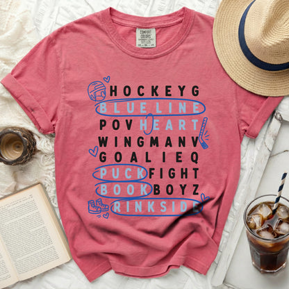 Pink t-shirt with hockey-themed words in blue and black.