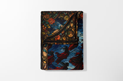 Folded blanket with stained glass design of roses and figures in red cloaks.