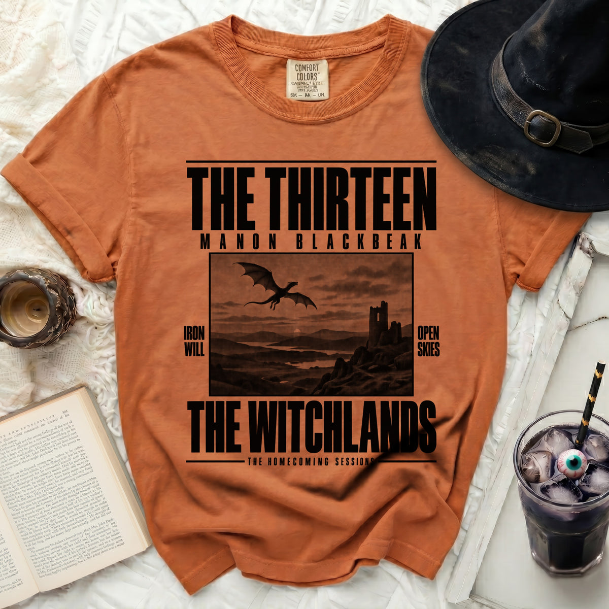 Orange t-shirt with "The Thirteen Manon Blackbeak" and "The Witchlands" text.