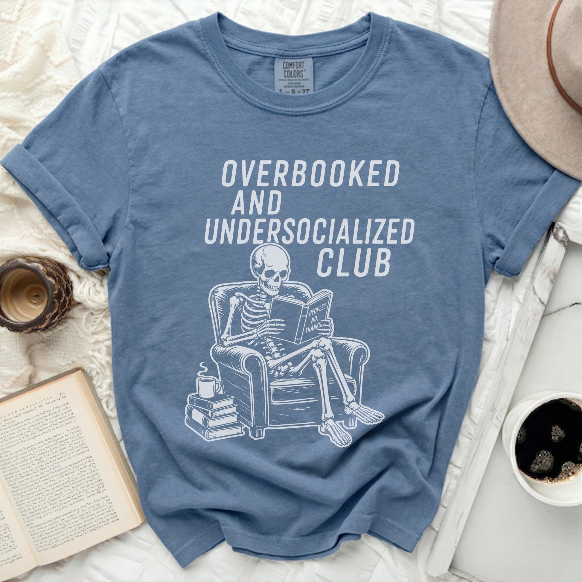 Skeleton sitting in chair, reading, with text Overbooked and Undersocialized Club.