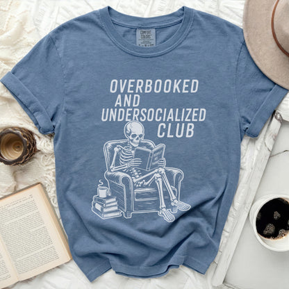 Skeleton sitting in chair, reading, with text Overbooked and Undersocialized Club.