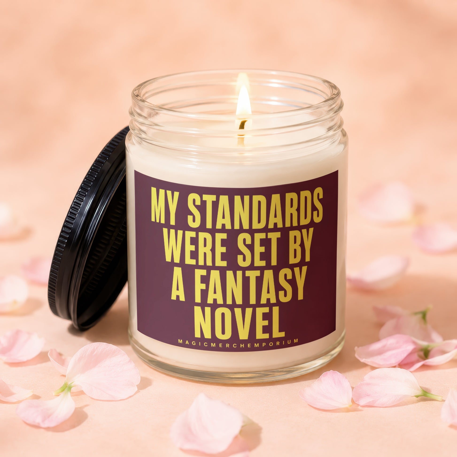 Glass candle with lit wick and label: "MY STANDARDS WERE SET BY A FANTASY NOVEL"