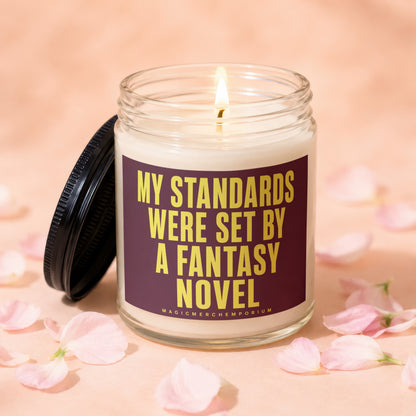 Glass candle with lit wick and label: "MY STANDARDS WERE SET BY A FANTASY NOVEL"
