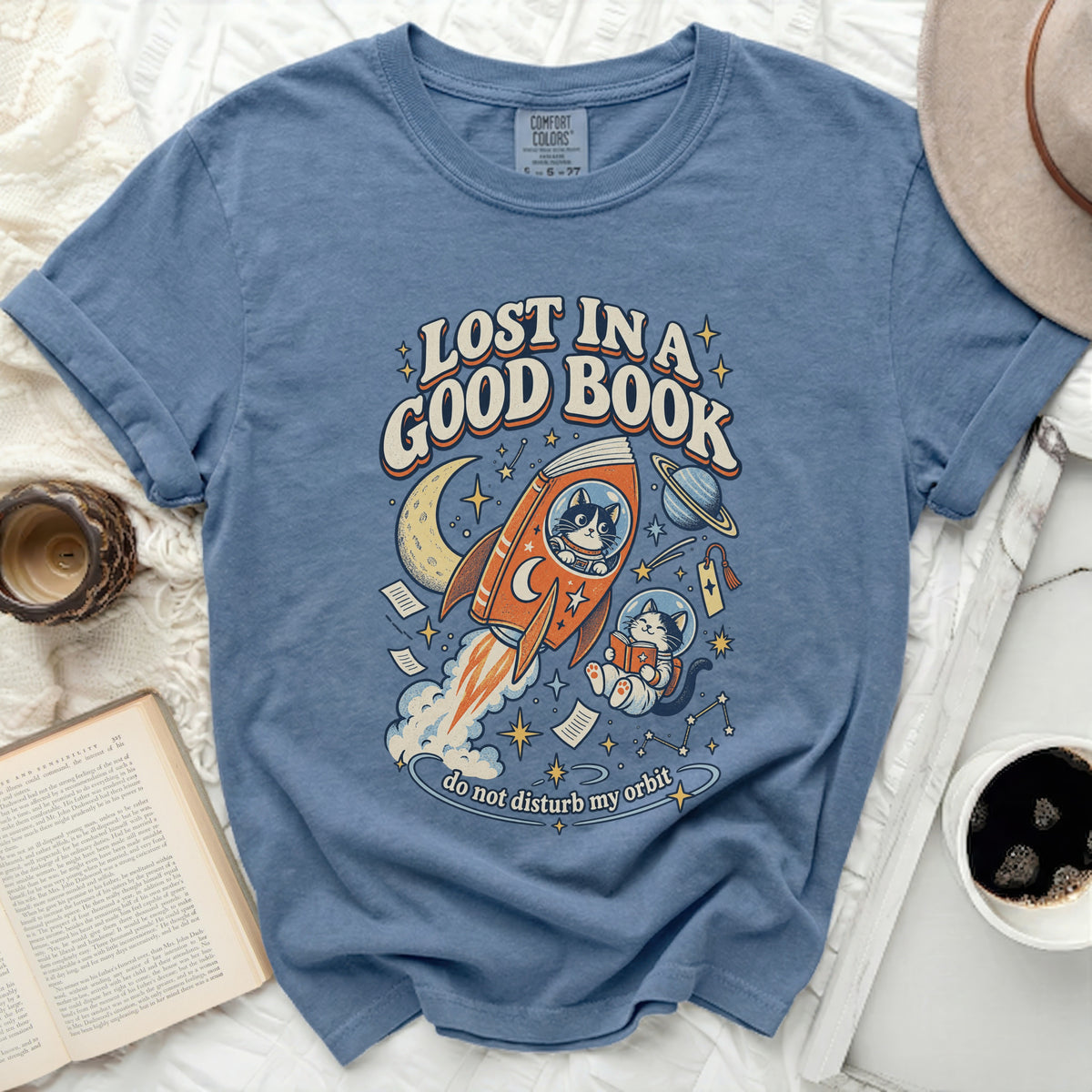 Blue t-shirt with "Lost in a Good Book" text and cats in space on a rocket.