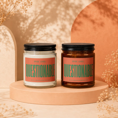 Two "Questionable" scented candles, one clear and one amber glass, on display.