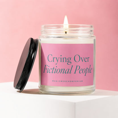 Glass jar candle with a lit wick and pink label reading "Crying Over Fictional People".