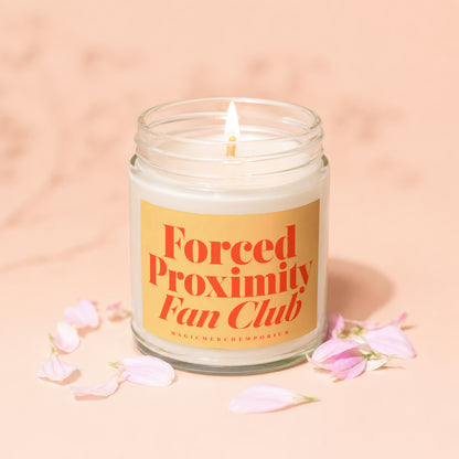 Lit candle in a glass jar with "Forced Proximity Fan Club" on the label.