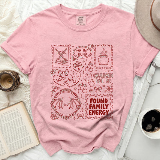 Pink t-shirt with red line art graphics of books, swords, cauldron, cherries, hearts, wings, and text.