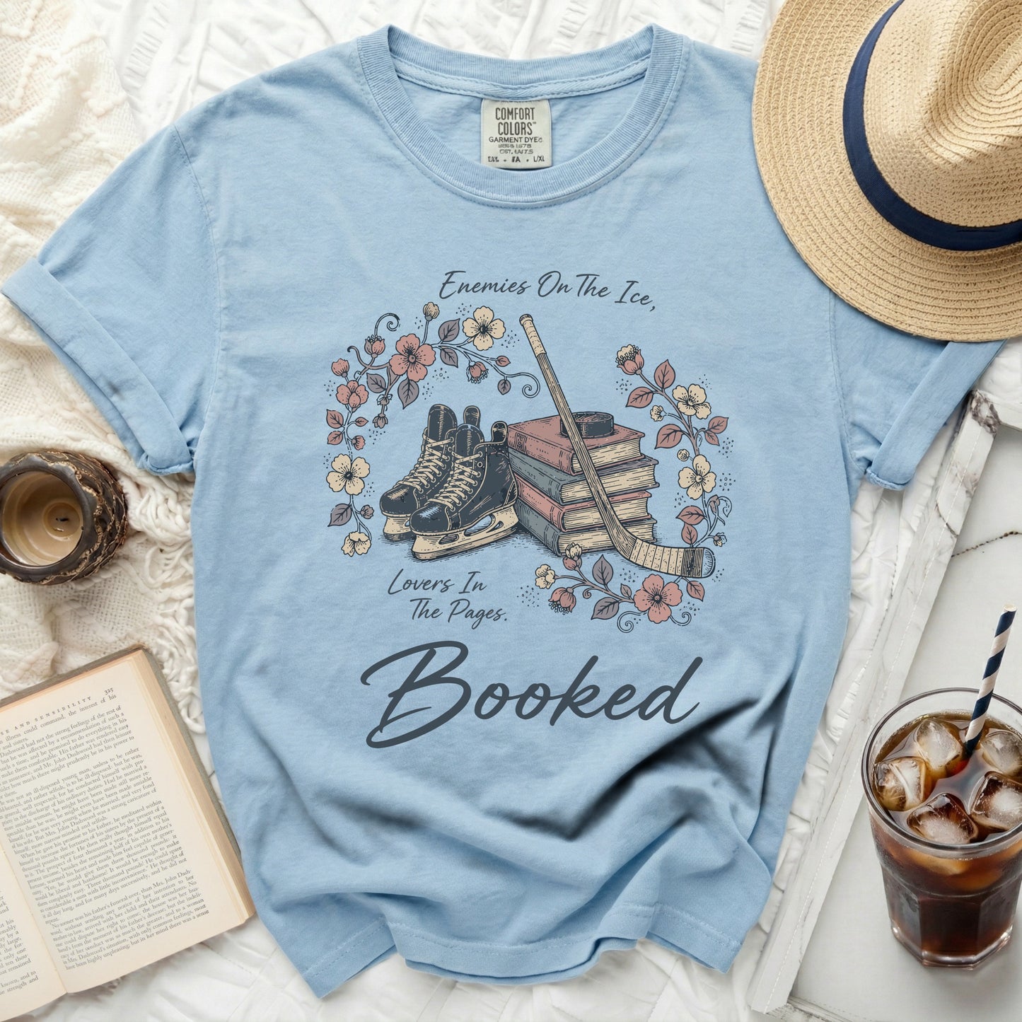 Light blue t-shirt with skates, books, and floral design, reading "Booked."