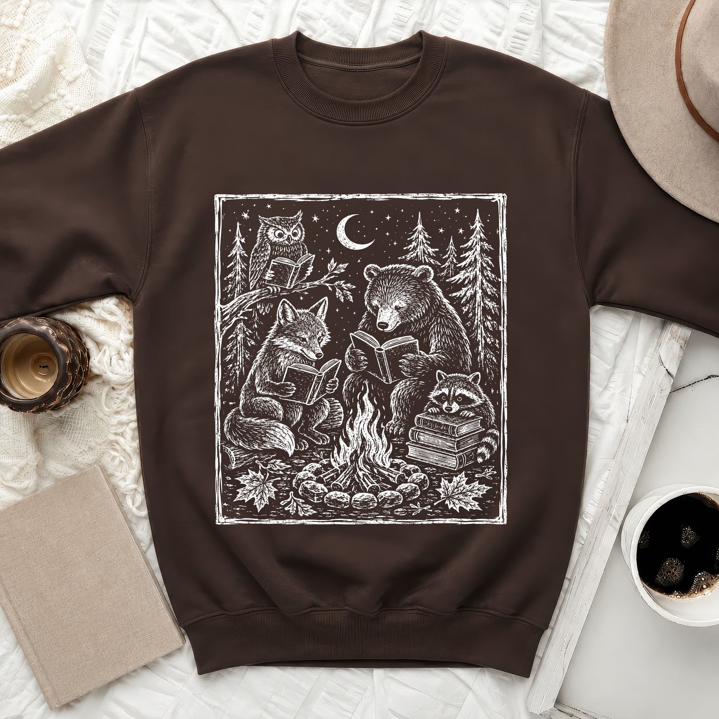 Brown sweatshirt with woodcut style print of forest animals reading by a campfire.
