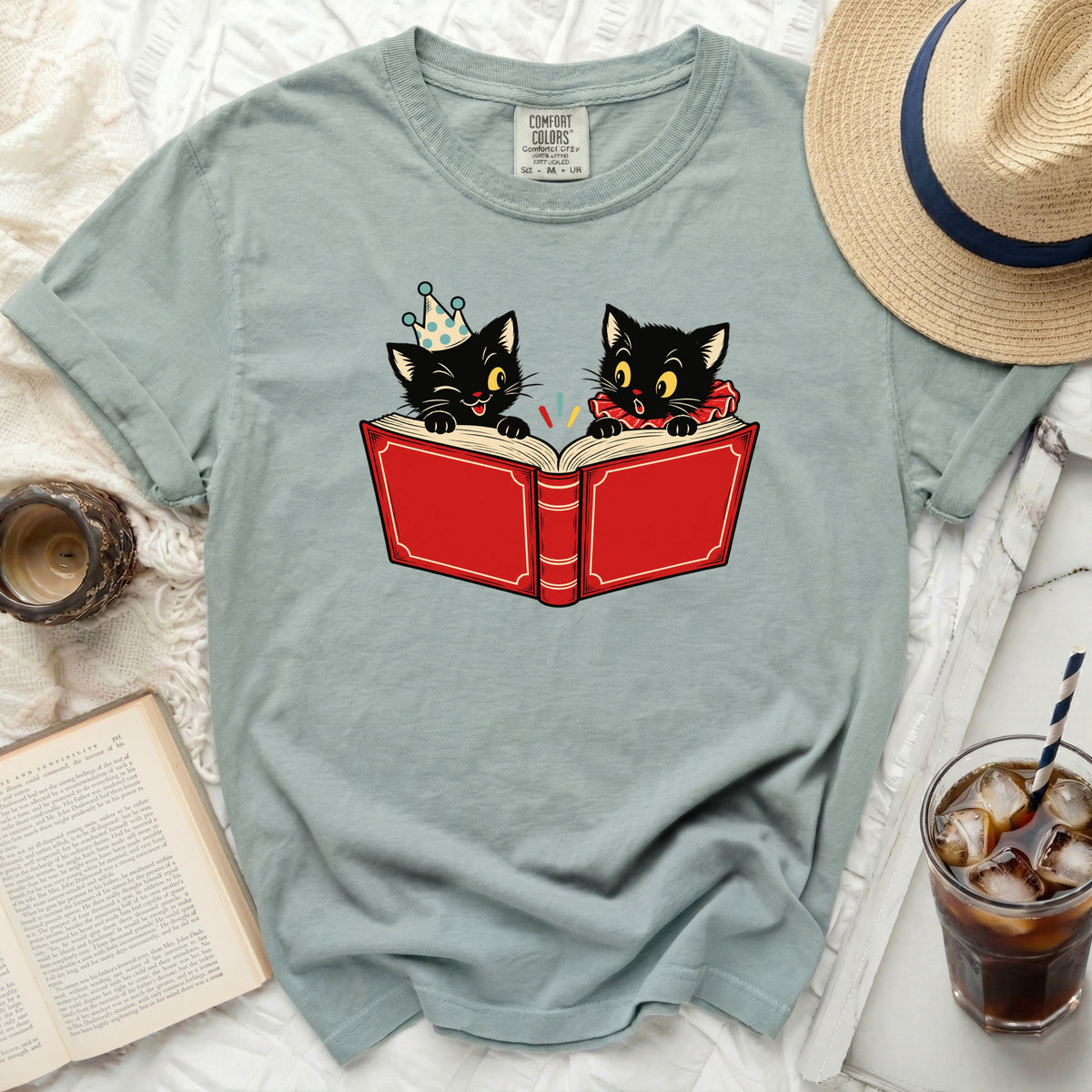 Two black cats read a book, one wearing a party hat and the other a ruff collar.
