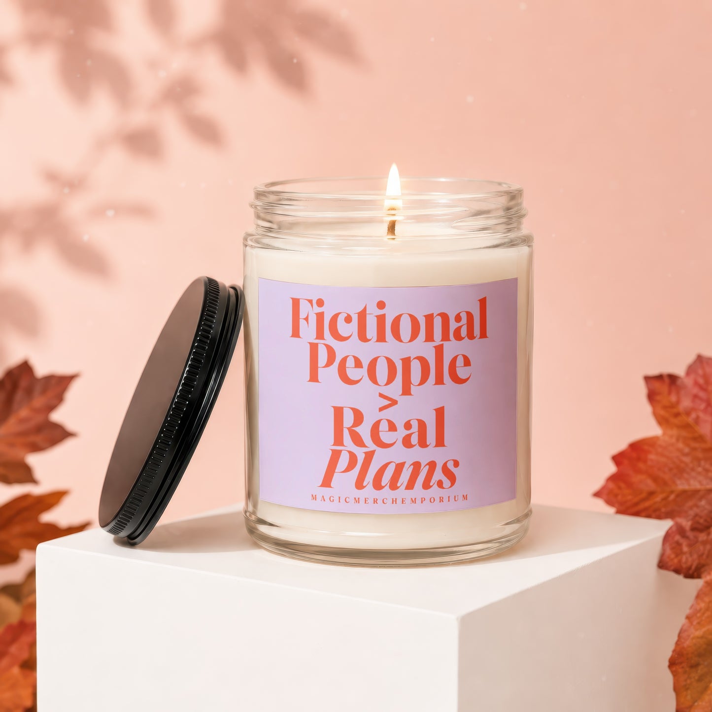 Lit candle with label "Fictional People Real Plans" on pedestal with autumn leaves.