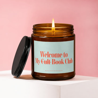 Amber glass candle with lit wick and black lid, reads "Welcome to My Cult Book Club".