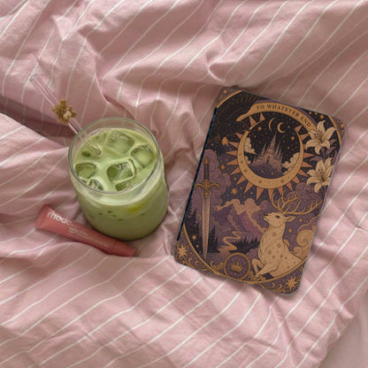 Green matcha drink, Rhode lip balm, and illustrative case on pink striped fabric.