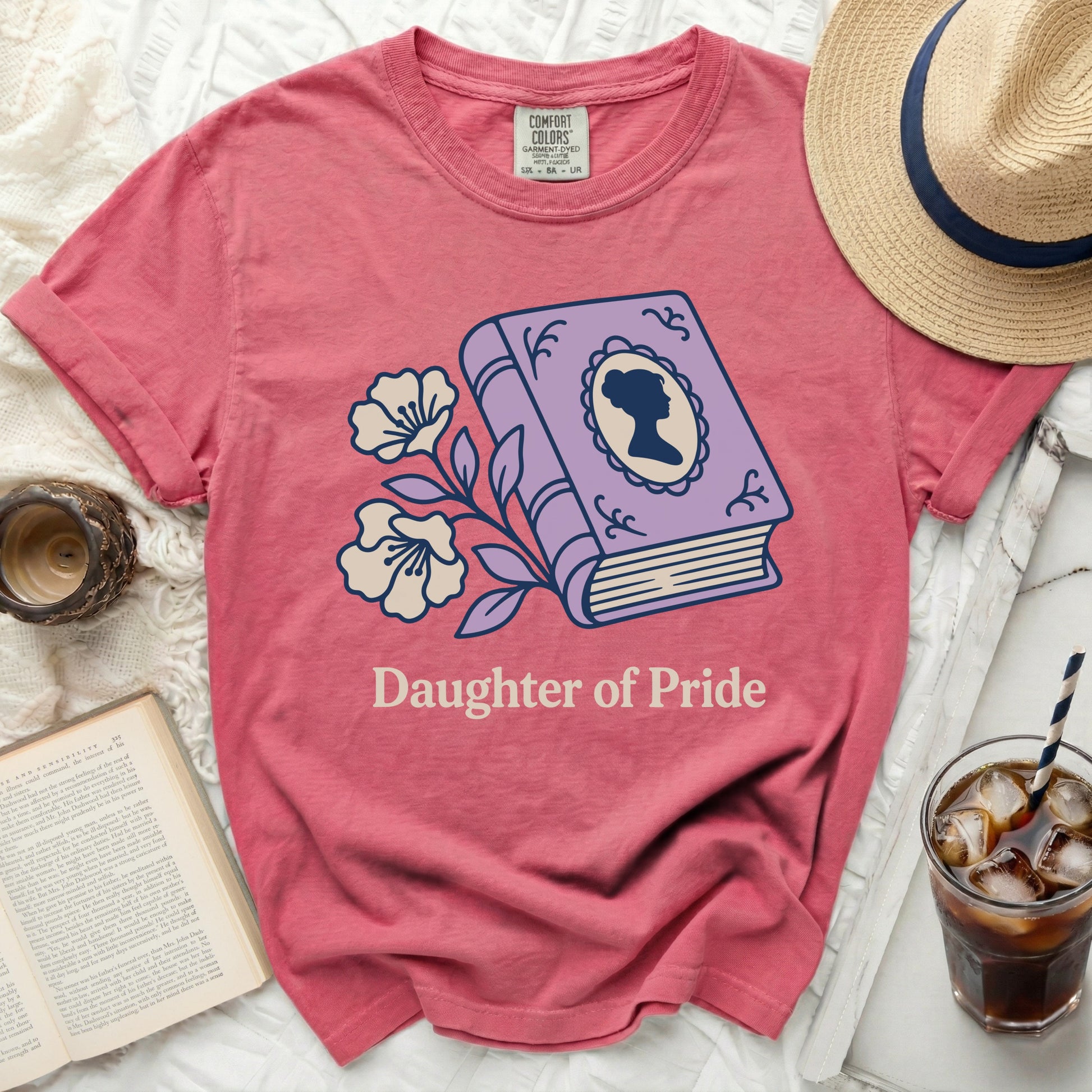 Pink t-shirt with "Daughter of Pride" and a book with a silhouette.