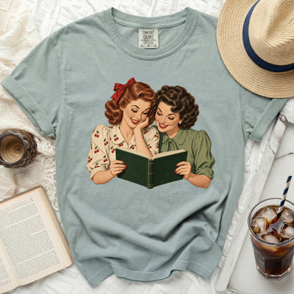 Two vintage-style women read a green book on a light blue t-shirt.