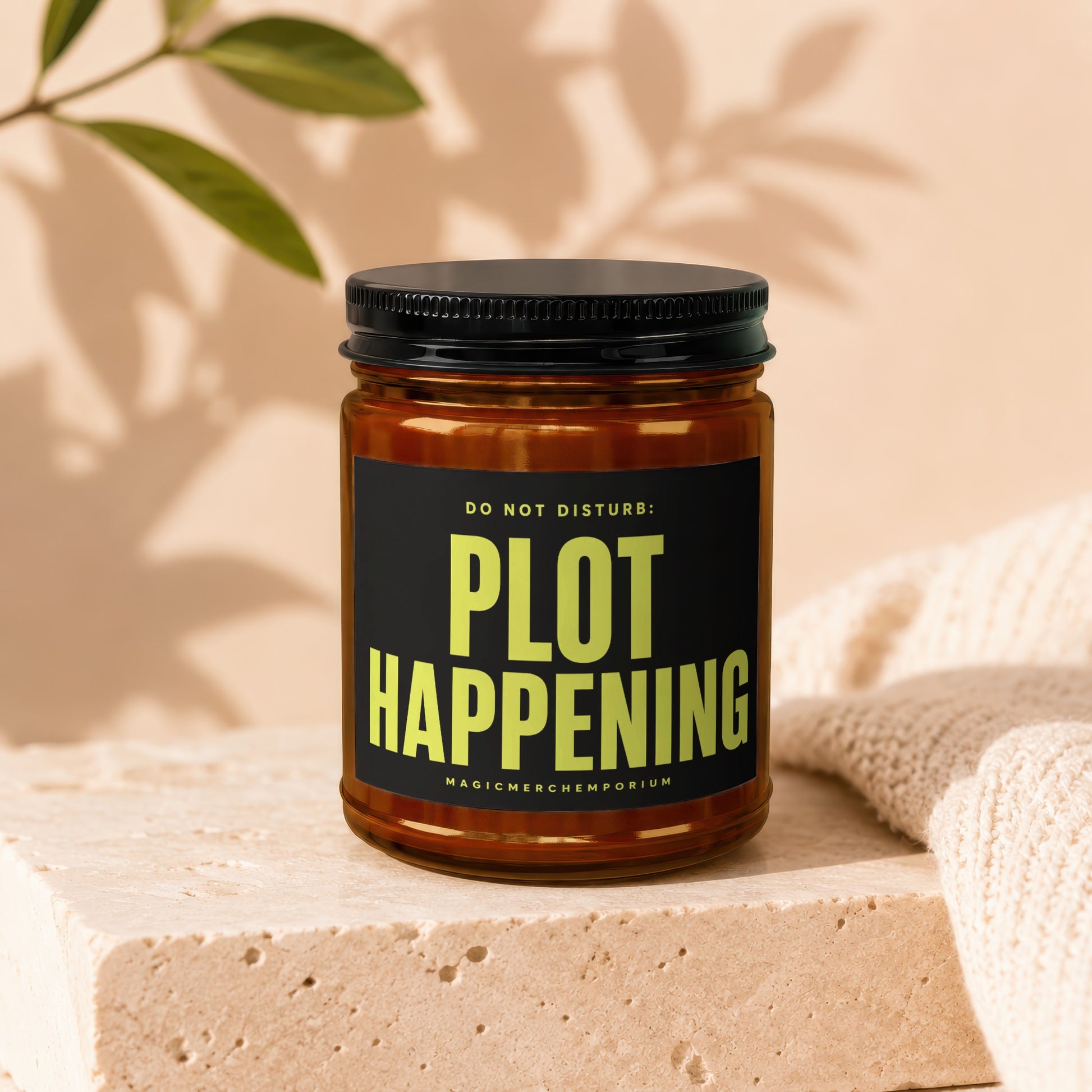 Brown glass candle with black lid, featuring "PLOT HAPPENING" text.