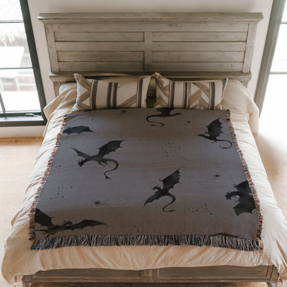 a bed with a gray blanket featuring black dragon silhouettes and stars. The bed has a wooden headboard and a striped pillow.