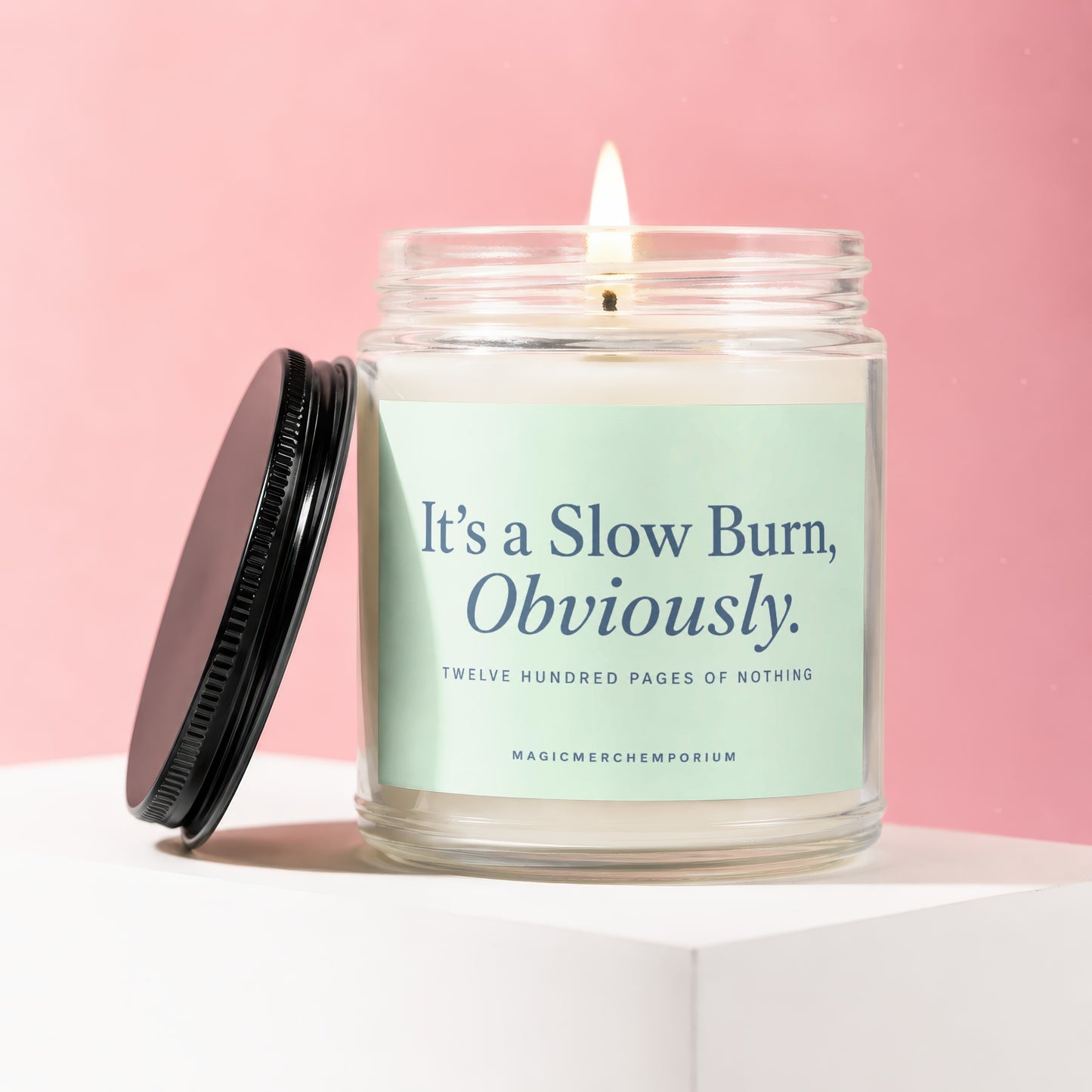 Lit candle with black lid and label reading "It's a Slow Burn, Obviously. TWELVE HUNDRED PAGES OF NOTHING".