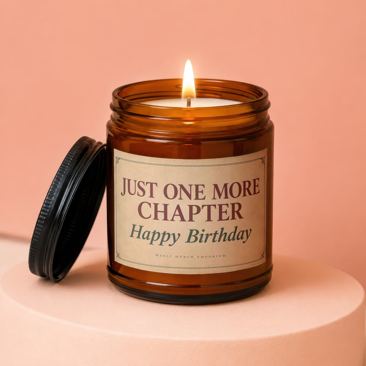 Amber jar candle with lit wick reads "Just One More Chapter, Happy Birthday."