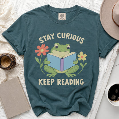 Teal t-shirt with a frog reading a book, surrounded by flowers and text.