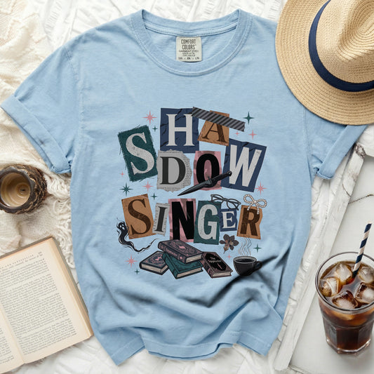 Light blue Comfort Colors t-shirt with "Shadow Singer" collage graphic and books.